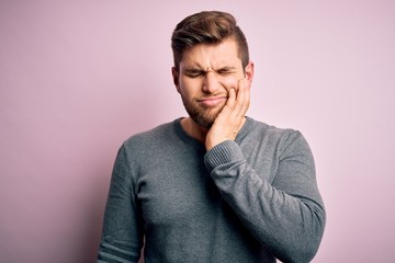 Young handsome blond man with beard and blue eyes wearing casual sweater touching mouth with hand with painful expression because of toothache or dental illness on teeth. Dentist