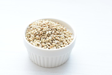 Raw barley grains, released in containers on white wooden background
