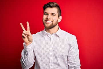 Young blond businessman with beard and blue eyes wearing elegant shirt over red background showing and pointing up with fingers number two while smiling confident and happy.