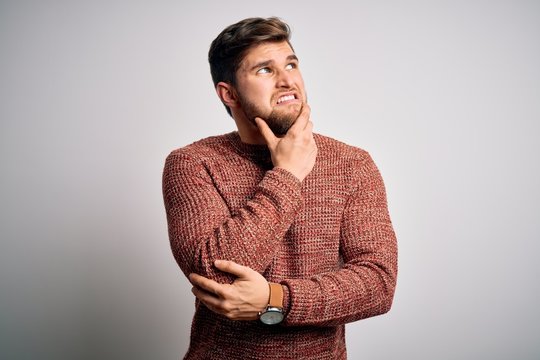 Young blond man with beard and blue eyes wearing casual sweater over white background Thinking worried about a question, concerned and nervous with hand on chin