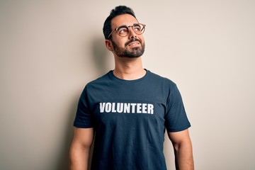 Handsome man with beard wearing t-shirt with volunteer message over white background smiling looking to the side and staring away thinking.
