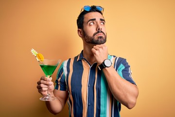 Young handsome tourist man with beard on vacation wearing summer shirt drinking cocktail serious...