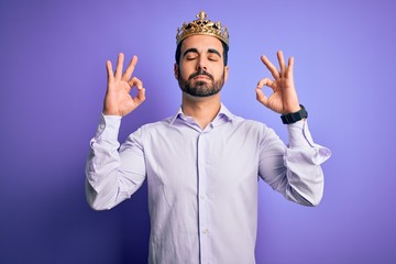 Young handsome man with beard wearing golden crown of king over purple background relax and smiling with eyes closed doing meditation gesture with fingers. Yoga concept.