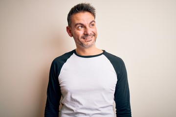 Young handsome man wearing casual t-shirt standing over isolated white background looking away to side with smile on face, natural expression. Laughing confident.