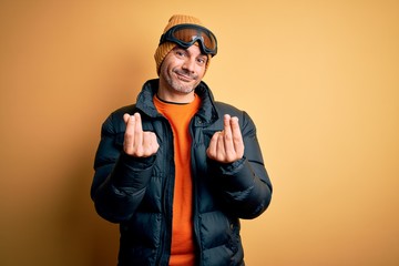 Young handsome skier man skiing wearing snow sportswear using ski goggles doing money gesture with...