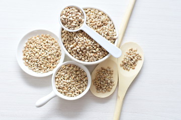 Raw barley grains, released in containers on white wooden background