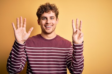 Young blond handsome man with curly hair wearing casual striped sweater showing and pointing up with fingers number eight while smiling confident and happy.