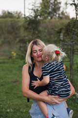 Obraz premium Mother gets kissed by blonde daugher in striped dress in park.