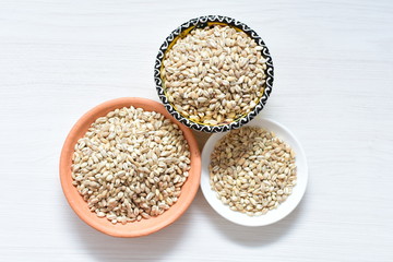 Raw barley grains, released in containers on white wooden background