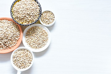 Raw barley grains, released in containers on white wooden background