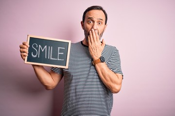 Middle age hoary man holding blackboard with smile message over isolated pink background cover...