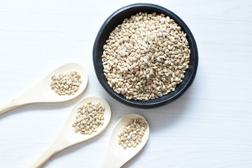 Raw barley grains, released in containers on white wooden background