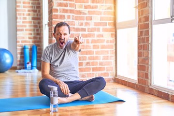 Middle age handsome sportman sitting on mat doing stretching yoga exercise at gym pointing displeased and frustrated to the camera, angry and furious with you