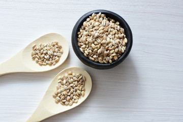 Raw barley grains, released in containers on white wooden background