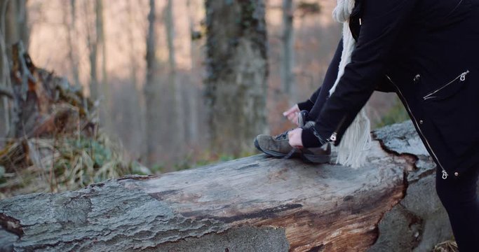 woman tying shoe on tree trunk
