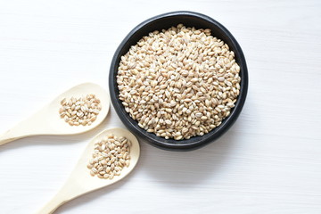 Raw barley grains, released in containers on white wooden background