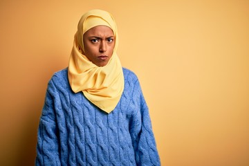 Young African American afro woman wearing muslim hijab over isolated yellow background skeptic and...