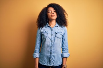 Young beautiful african american woman with afro hair standing over yellow isolated background Relaxed with serious expression on face. Simple and natural looking at the camera.