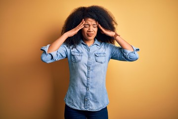 Young beautiful african american woman with afro hair standing over yellow isolated background with hand on head for pain in head because stress. Suffering migraine.