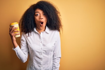 Young african american business woman with afro hair drinking coffee from take away cup scared in shock with a surprise face, afraid and excited with fear expression