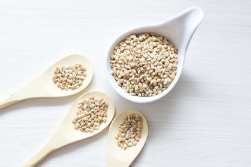 Raw barley grains, released in containers on white wooden background
