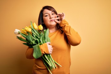 Beautiful plus size woman holding romantic bouquet of natural tulips flowers over yellow background...