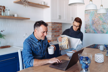 Men using laptop and driking coffee at home and talking with his wife