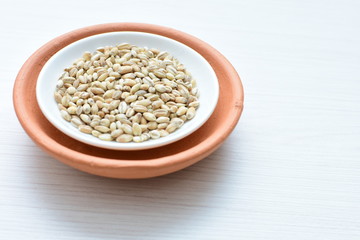 Raw barley grains, released in containers on white wooden background