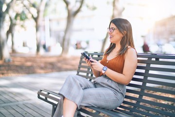 Young beautiful woman smiling happy and confident. Sitting with smile on face using smartphone at the city