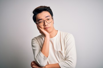 Young handsome chinese man wearing casual t-shirt and glasses over white background thinking looking tired and bored with depression problems with crossed arms.