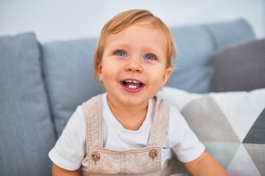 Adorable blonde toddler sitting on the sofa smiling happy at home