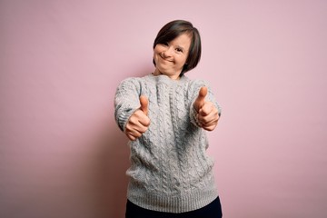 Young down syndrome woman wearing casual sweater over isolated background approving doing positive...