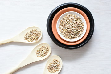 Raw barley grains, released in containers on white wooden background