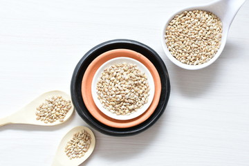 Raw barley grains, released in containers on white wooden background