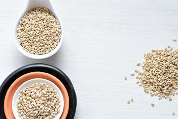 Raw barley grains, released in containers on white wooden background