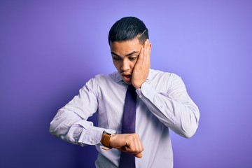 Young brazilian businessman wearing elegant tie standing over isolated purple background Looking at the watch time worried, afraid of getting late