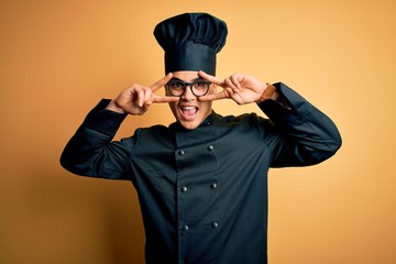 Young brazilian chef man wearing cooker uniform and hat over isolated yellow background Doing peace...