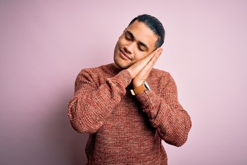 Young brazilian man wearing casual sweater standing over isolated pink background sleeping tired dreaming and posing with hands together while smiling with closed eyes.