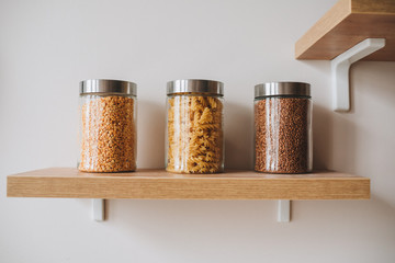 Three jars with pasta,bulgur, buckwheat on shelf as healthy foods