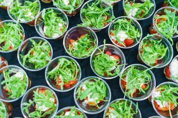 Mini appetizer salad in a glass of tomatoes with mozzarella, arugula and pesto. Italian traditional food for guests and participants at the event. Catering and guest services.