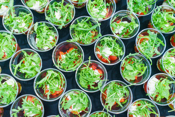 Mini appetizer salad in a glass of tomatoes with mozzarella, arugula and pesto. Italian traditional food for guests and participants at the event. Catering and guest services.