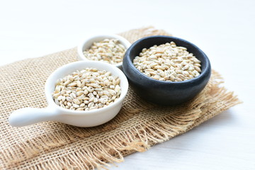 Raw barley grains, displayed in containers on textured background