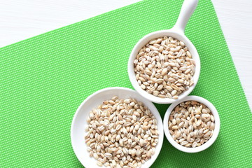Raw barley grains, displayed in containers on textured background