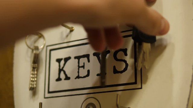 Person hanging House Keys on a hook key holder on the wall. 