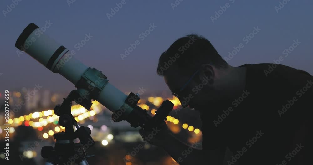 Wall mural astronomer with a telescope watching at the stars and moon with blurred city lights in the backgroun