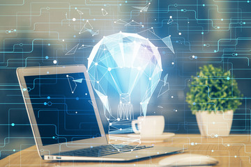 Computer on desktop in office with bulb icon hologram. Multi exposure. Concept of idea.