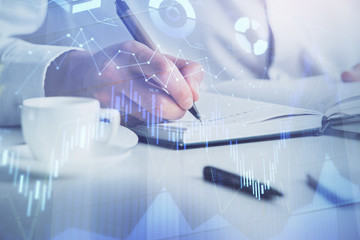 Double exposure of man's hands writing notes of stock market with forex chart.