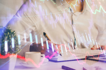 Double exposure of man's hands writing notes of stock market with forex chart.