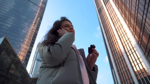Girl pulls out and puts on wireless headphones among the skyscrapers