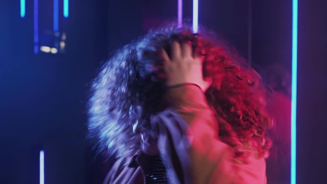 80s style girl. Clubbing lifestyle. Amused woman with curly hair dancing in blue pink red neon glow.